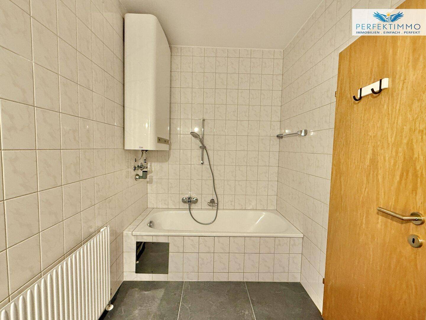 Gefliestes Badezimmer mit Badewanne und Boiler, einfach und praktisch eingerichtet.