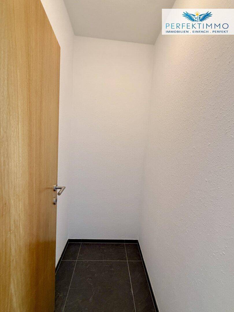 Kleiner Abstellraum mit dunklem Fliesenboden und weiß gestrichenen Wänden.