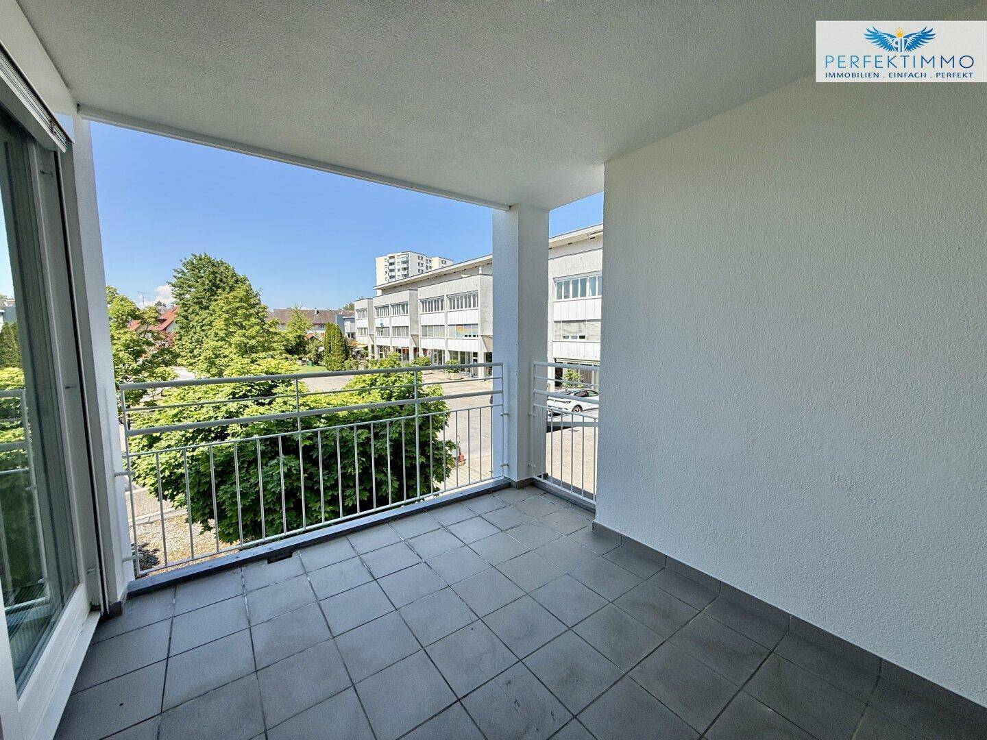 Heller Balkon mit Fliesenboden und weitem Blick auf die umliegenden Gebäude und Grünflächen.