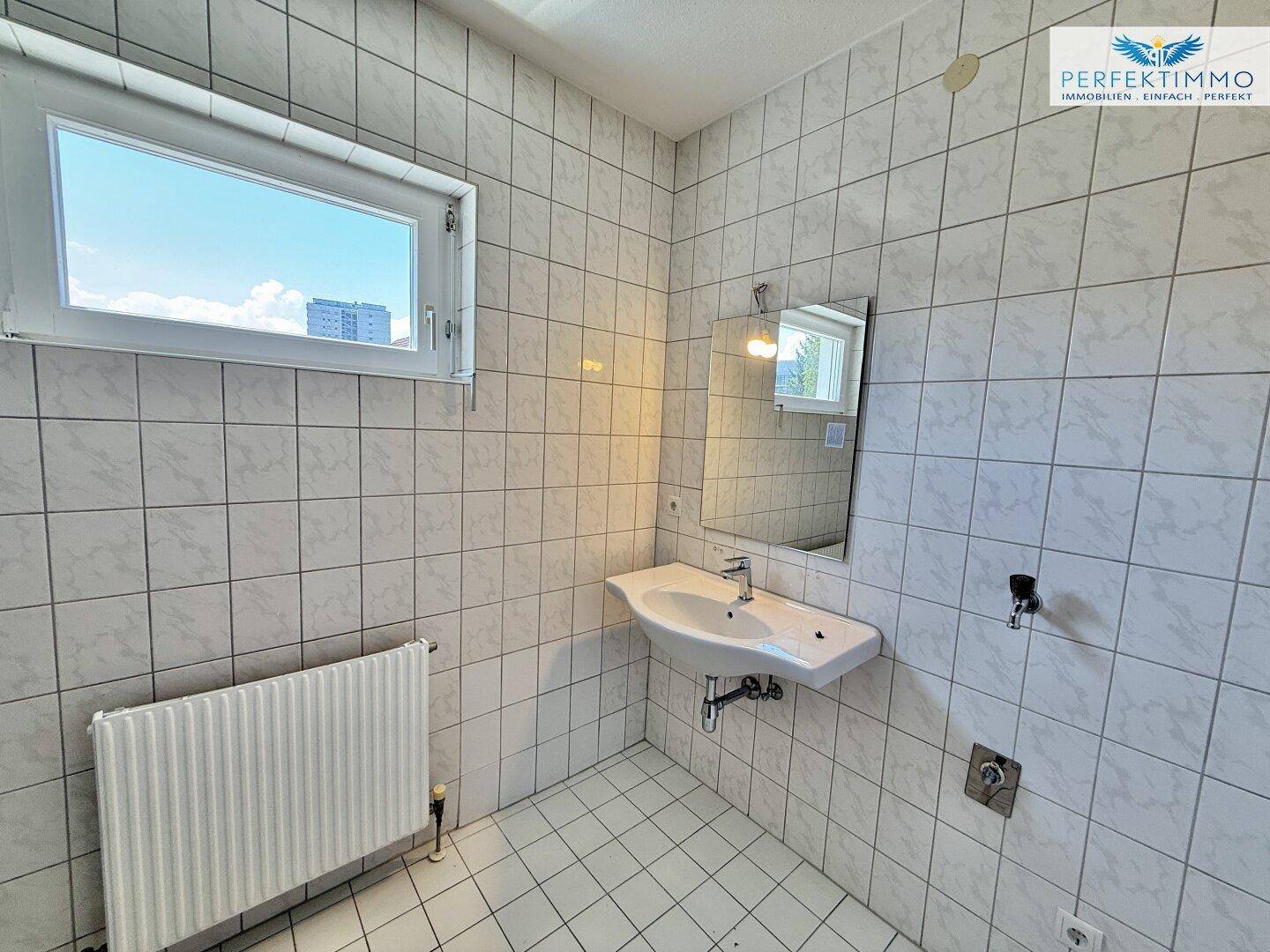 Gefliestes Badezimmer mit Waschbecken, Spiegel und Fenster für Tageslicht.