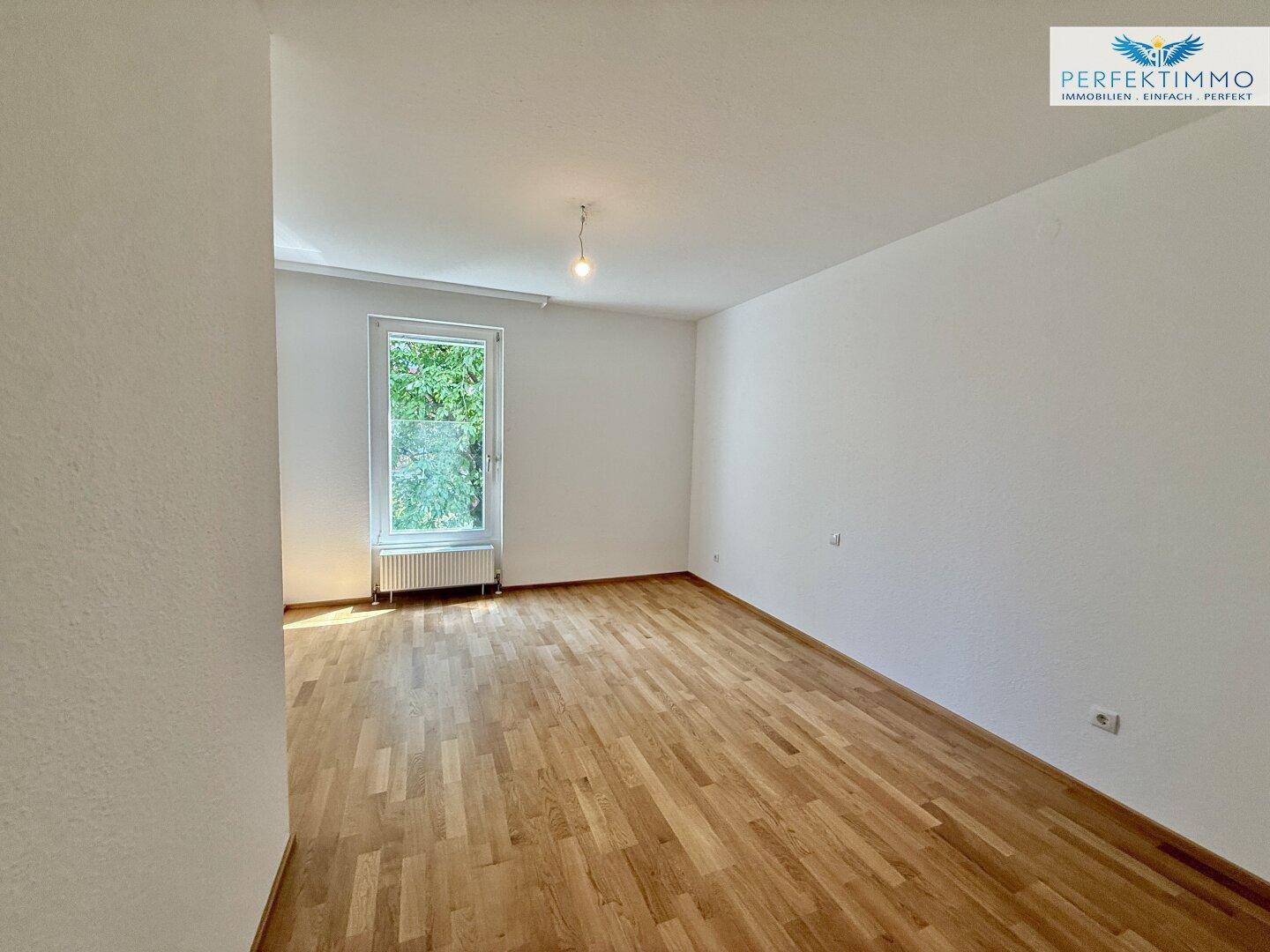 Helles Schlafzimmer mit Holzboden und einem Fenster, das viel Tageslicht hereinlässt.
