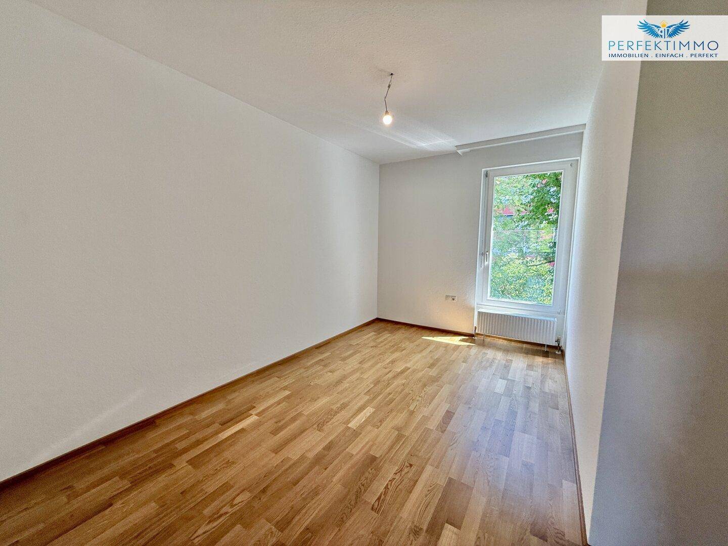 Helles Zimmer mit Holzboden und einem Fenster, ideal als Schlaf- oder Arbeitszimmer.