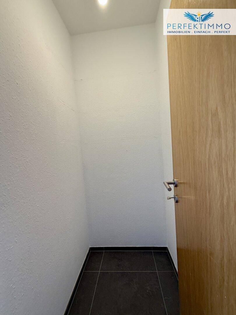 Praktischer Abstellraum mit dunklem Fliesenboden und weißen Wänden.