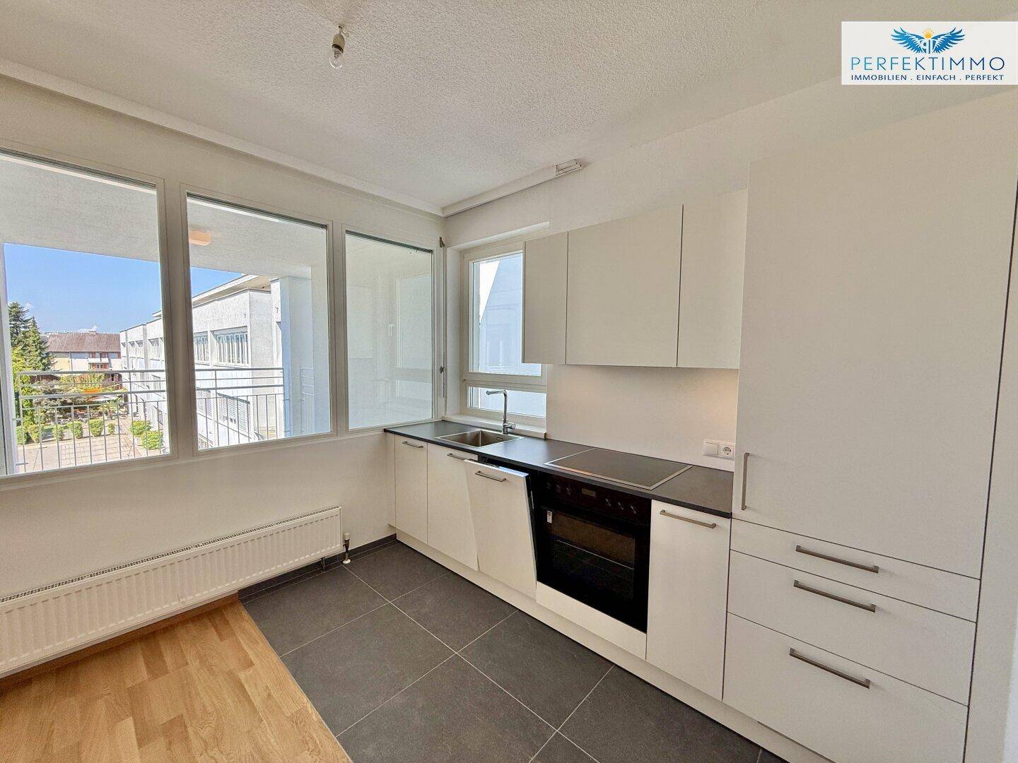Moderne Einbauküche mit weißen Schränken, dunkler Arbeitsplatte und Fenster mit Ausblick.
