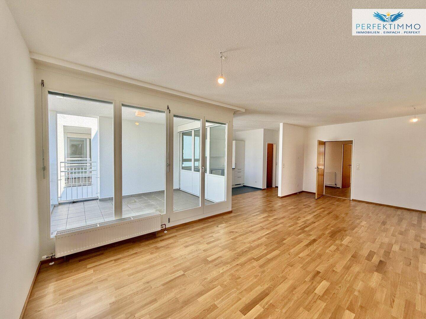 Heller Wohnbereich mit Parkettboden und Zugang zu einem verglasten Balkon.