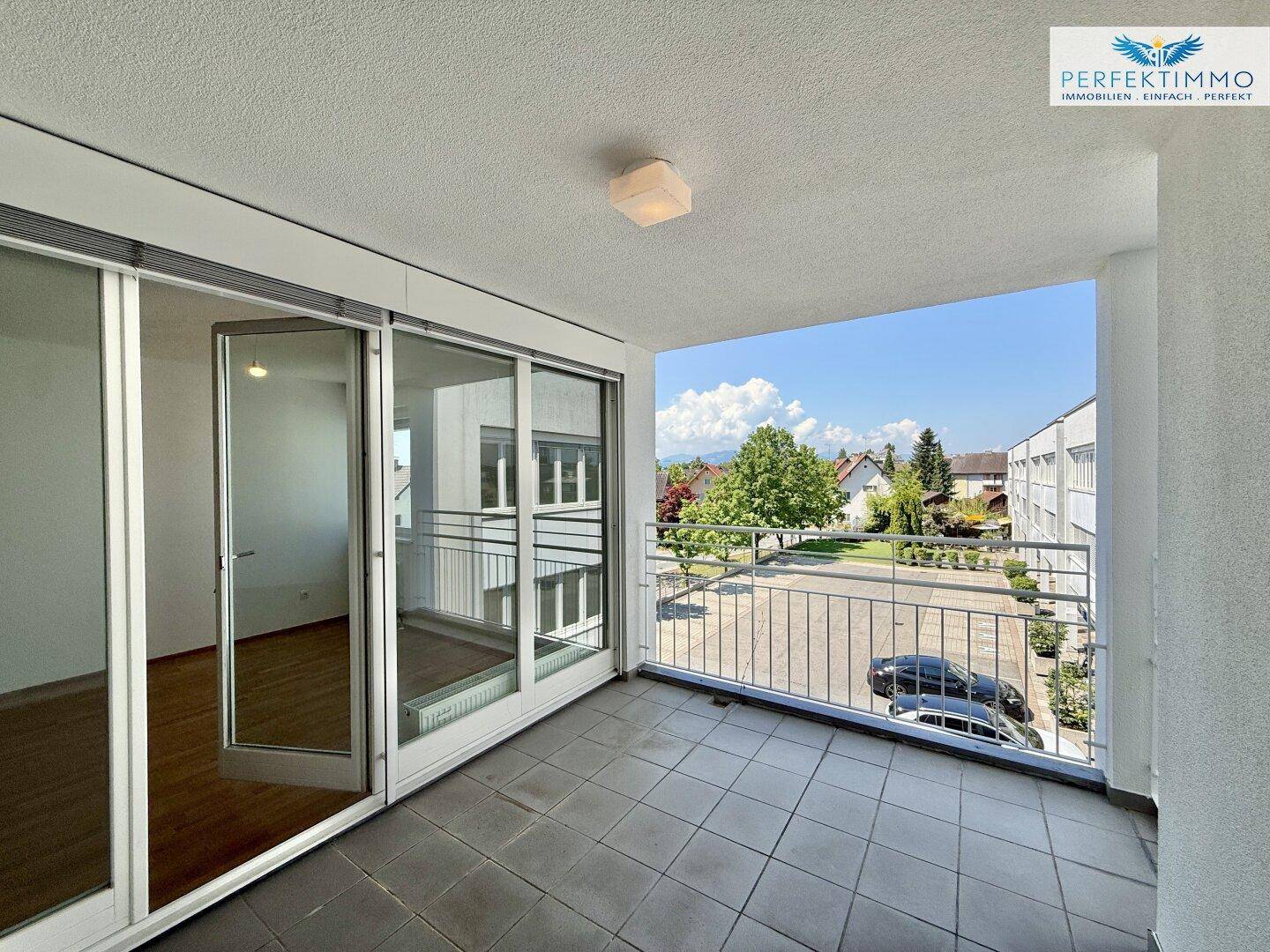 Geräumiger Balkon mit Fliesenboden und Blick auf die Umgebung und Parkplätze.