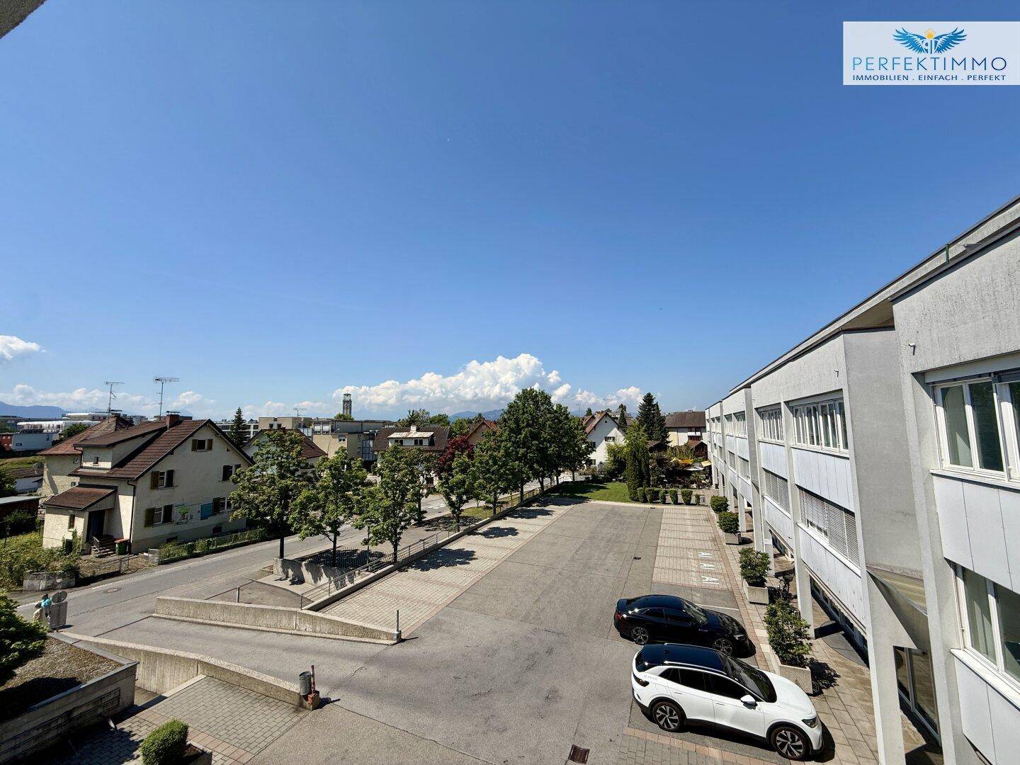 Weitläufiger Blick über die Umgebung mit Gebäuden, Bäumen und einem klaren blauen Himmel.