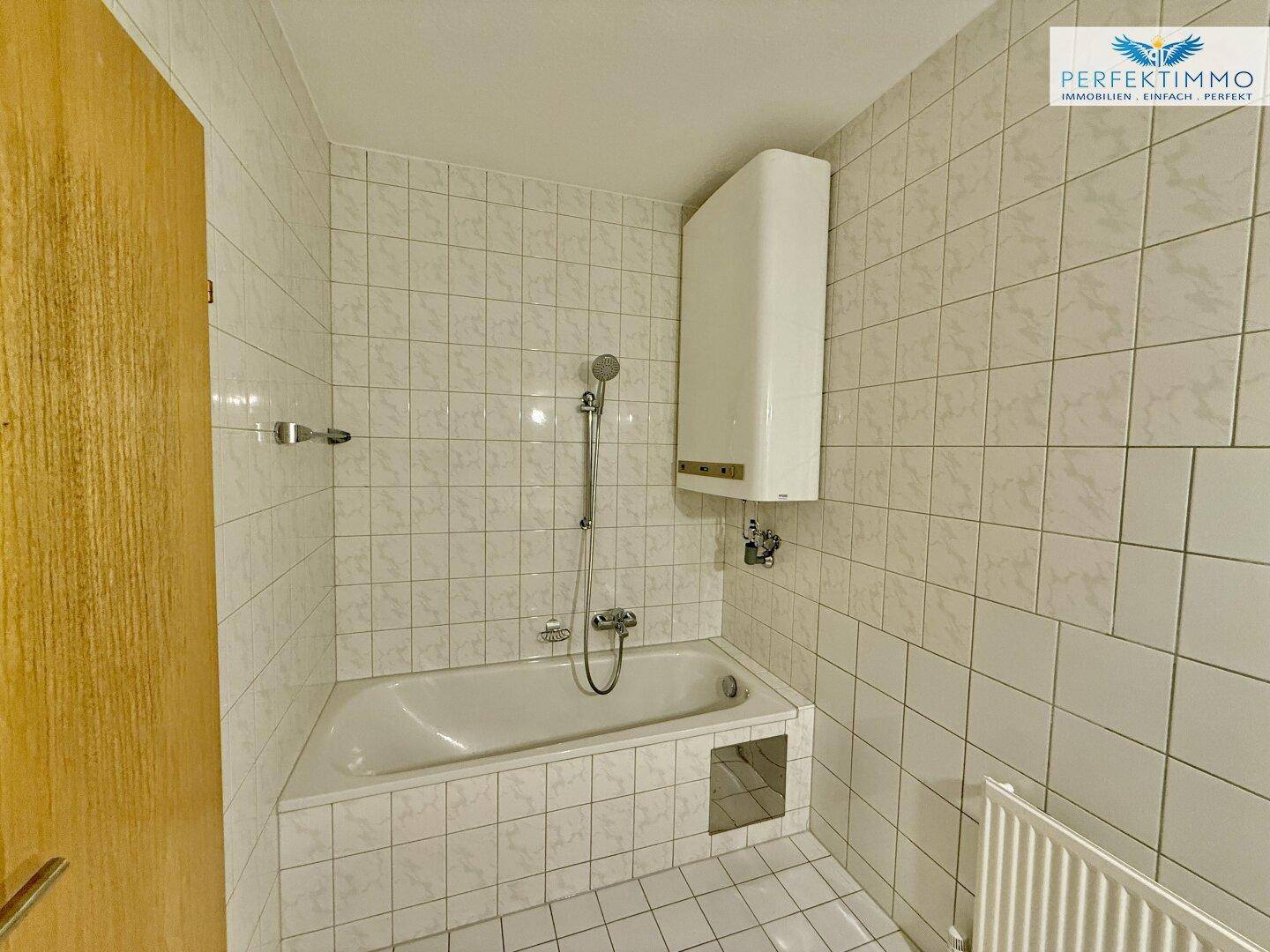 Gefliestes Badezimmer mit Badewanne und Duscharmatur, in einem gepflegten Zustand.