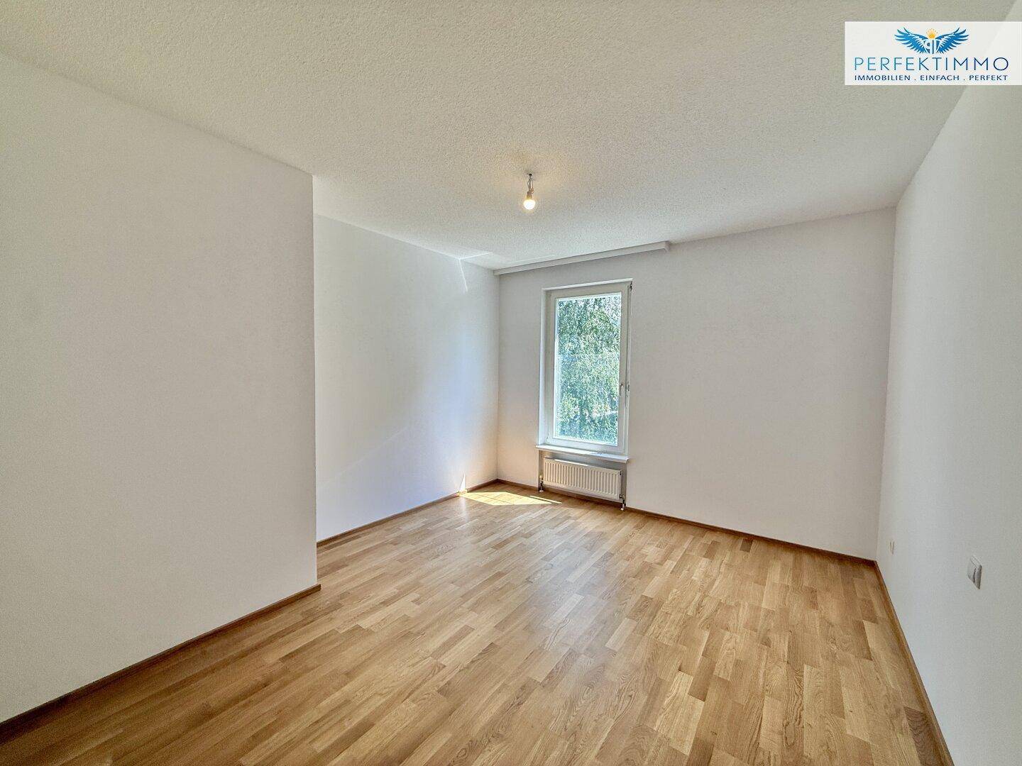 Geräumiges Schlafzimmer mit Parkettboden und einem Fenster, das eine grüne Aussicht bietet.