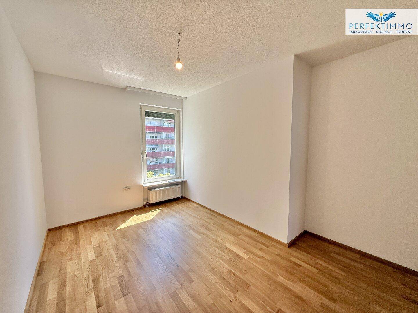 Geräumiges Schlafzimmer mit Parkettboden und einem Fenster, das eine grüne Aussicht bietet.