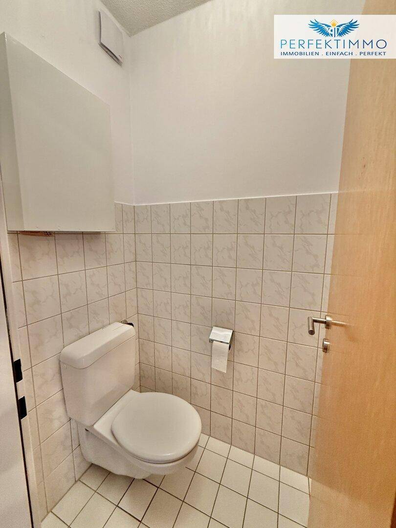Kleines Gäste-WC mit Toilette und Fliesen an den Wänden, in hellem Zustand.