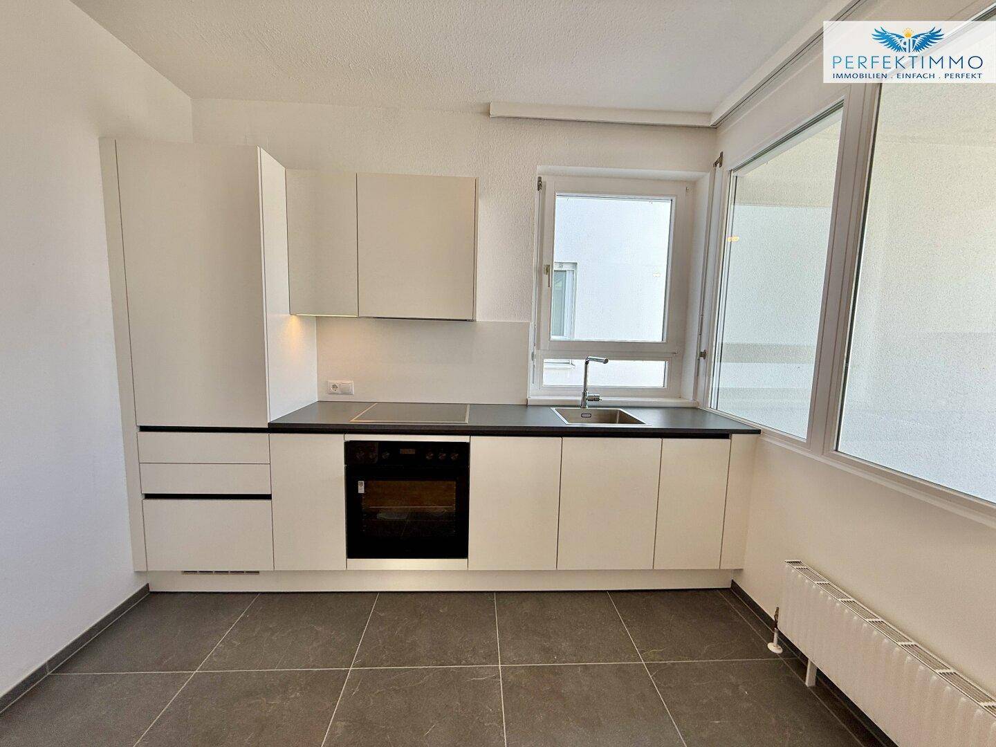Helle Einbauküche mit weißen Fronten, integriertem Backofen und Fenster.