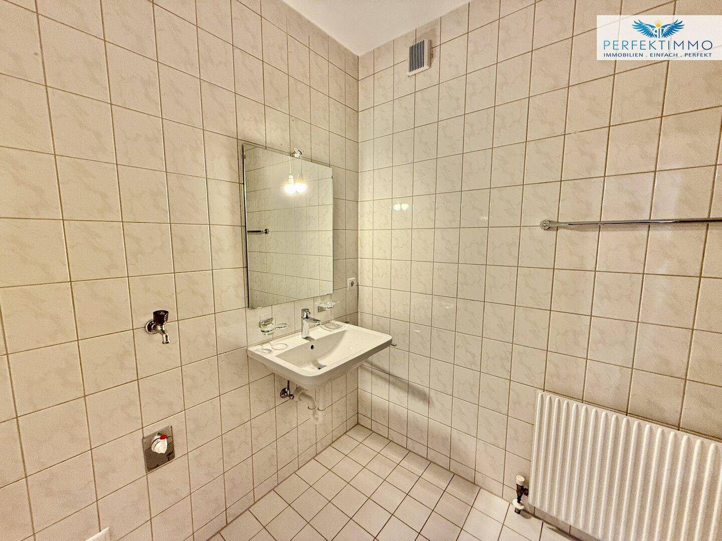 Gefliestes Badezimmer mit Waschbecken, Spiegel und Heizkörper.