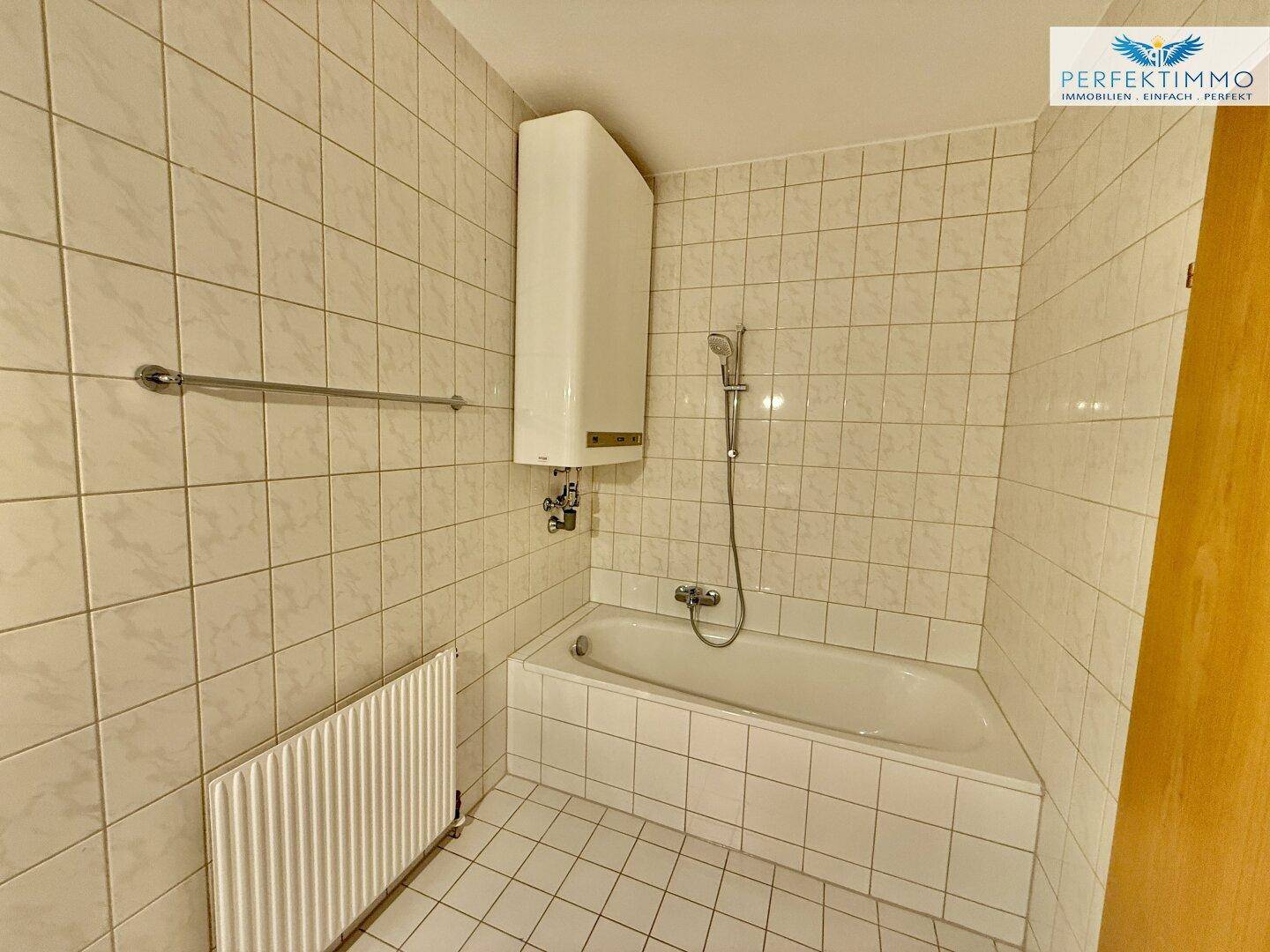 Badezimmer mit Badewanne, Fliesen an den Wänden und Warmwasserboiler.