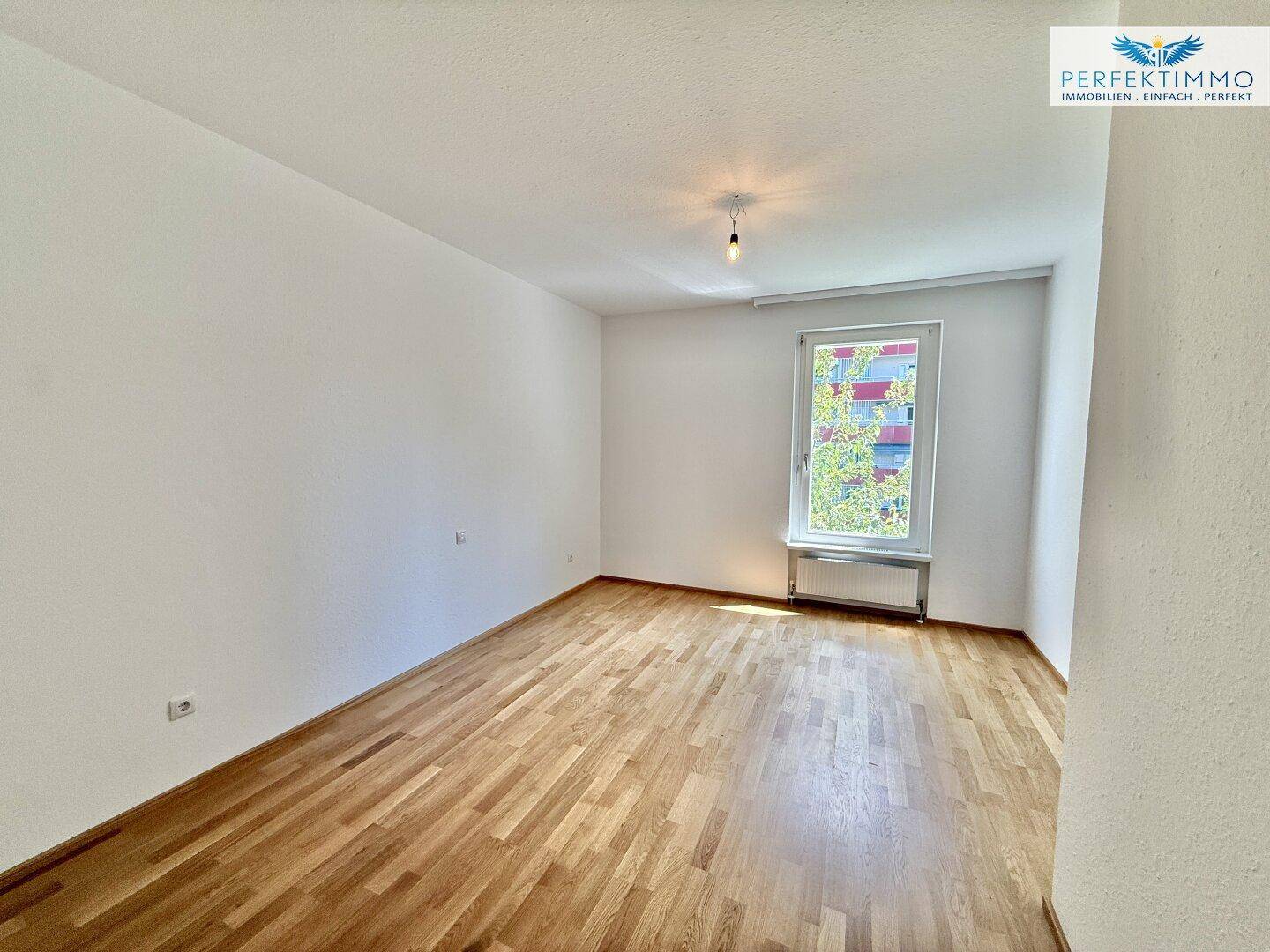 Helles Schlafzimmer mit Parkettboden und einem Fenster zur Außenseite.
