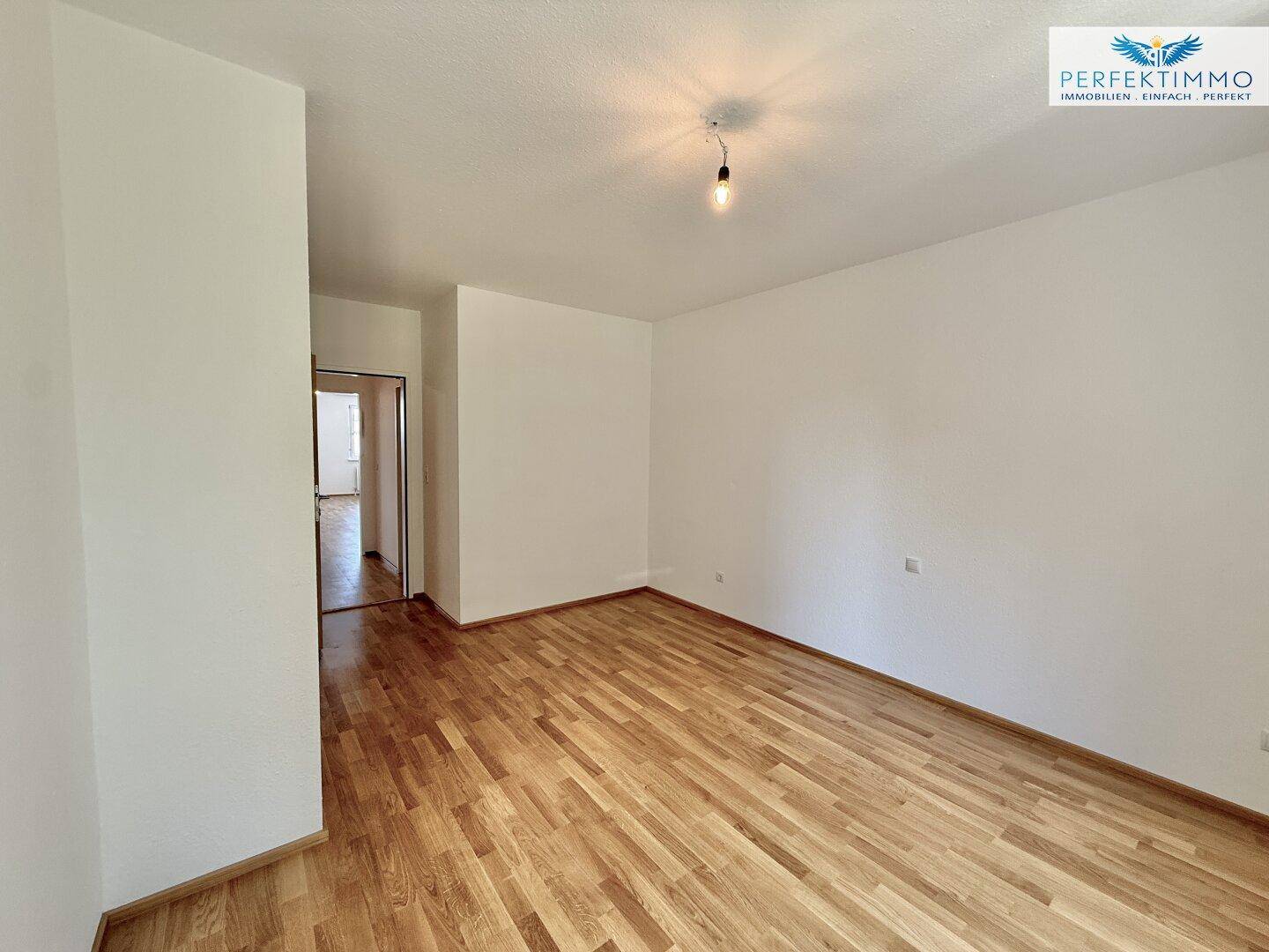 Helles Zimmer mit Parkettboden und weiß gestrichenen Wänden.