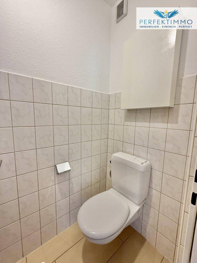 Separate Toilette mit Fliesen an den Wänden und einem wandhängenden WC.