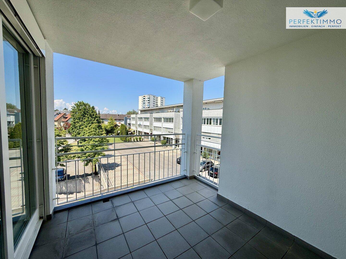 Geräumiger Balkon mit Fliesenboden und Blick auf die umliegenden Gebäude und grüne Bäume.