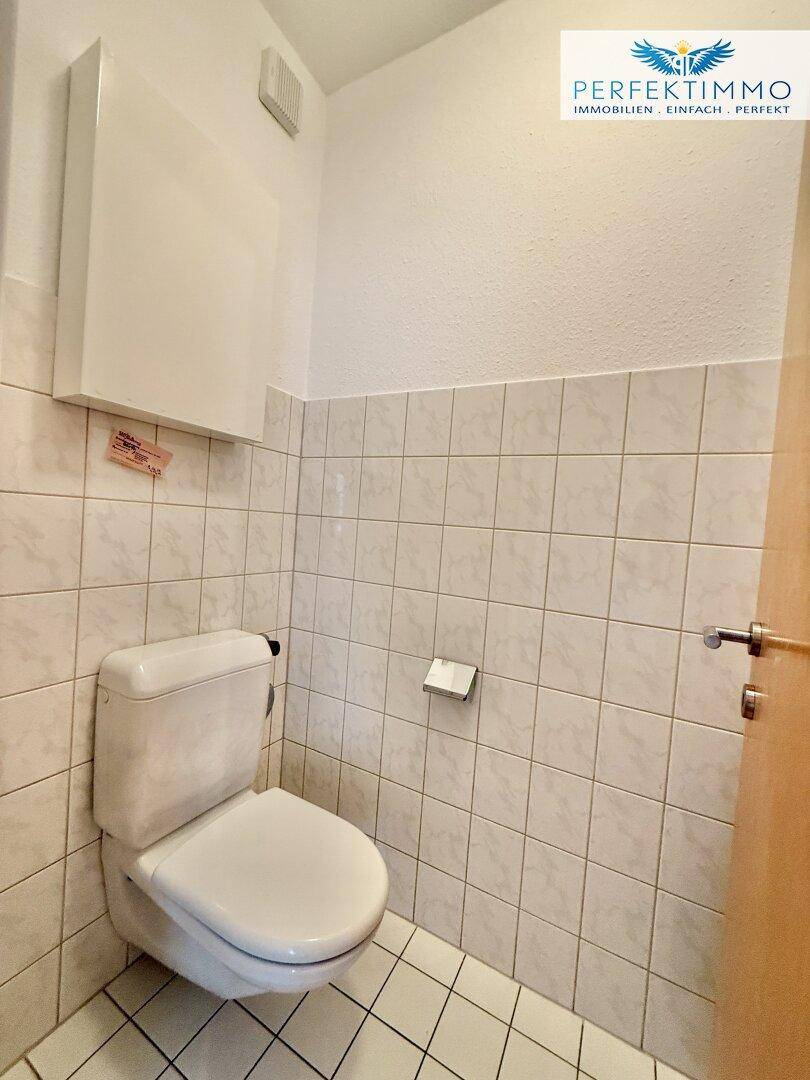 Separates WC mit weißen Fliesen an Wänden und Boden, ausgestattet mit einer Standardtoilette.