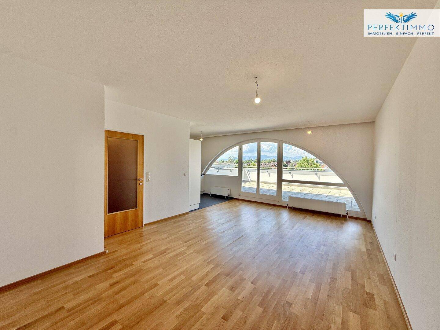 Heller Wohnbereich mit Parkettboden und großen Bogenfenstern zur Terrasse.