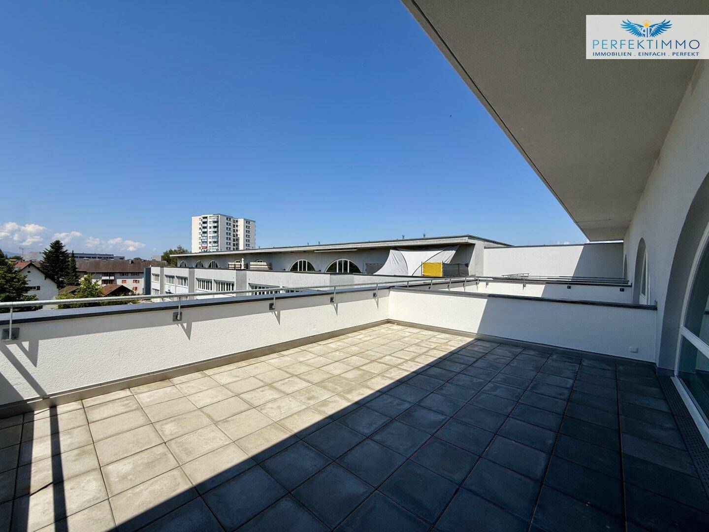 Helle Dachterrasse mit Fliesenboden und Blick auf die umliegenden Gebäude.