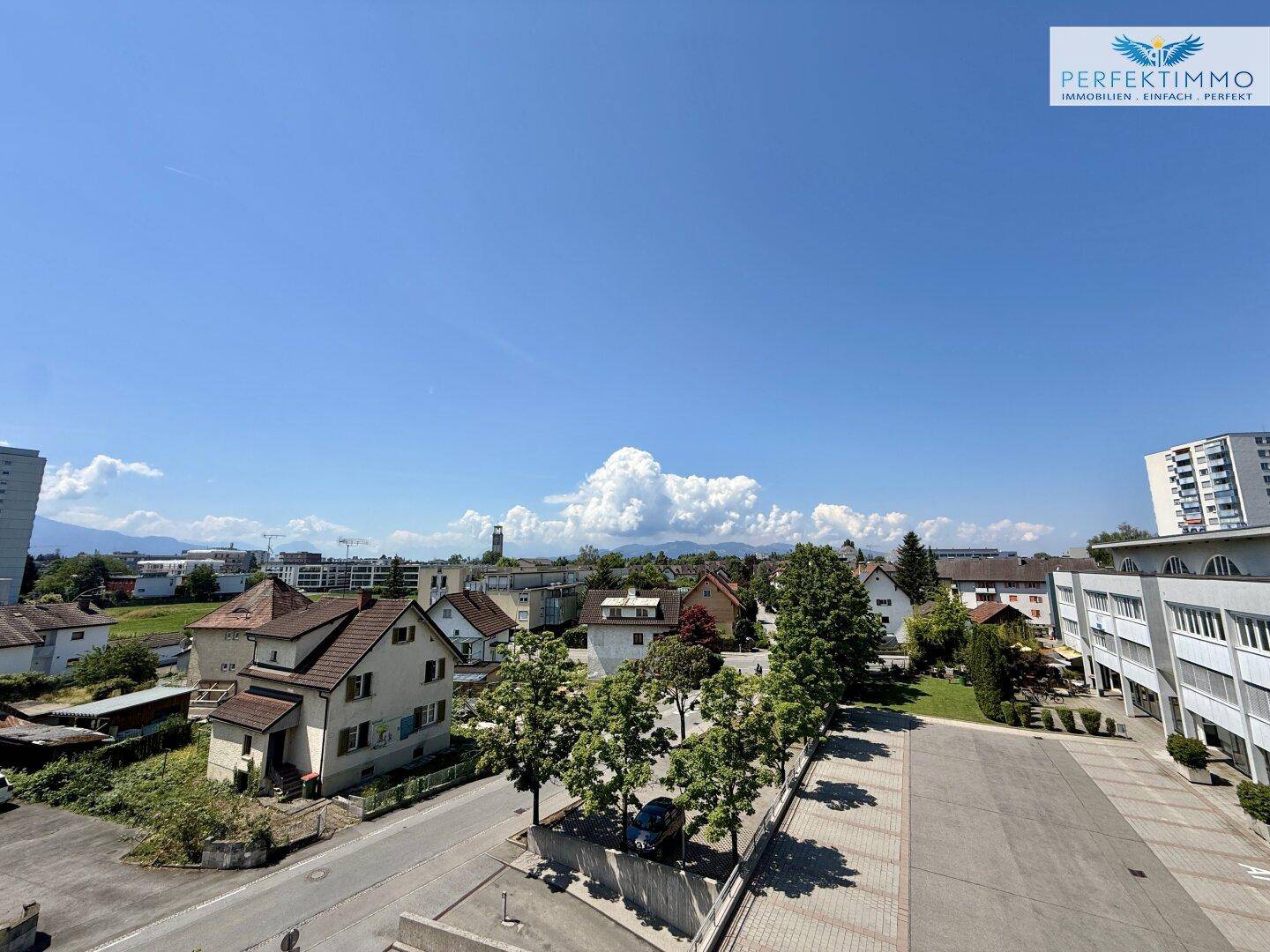 Weitläufiger Blick über die Stadt und die umliegende Landschaft unter blauem Himmel.