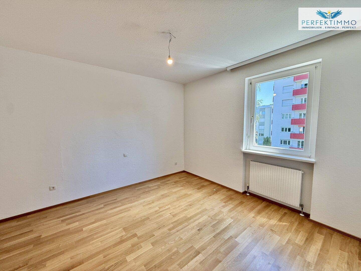 Helles Schlafzimmer mit Parkettboden und Fenster mit Blick auf die Umgebung.
