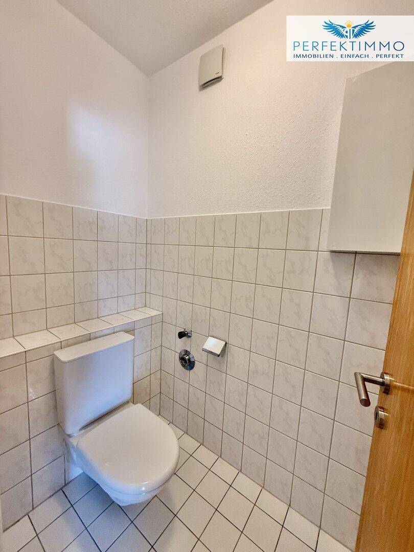 Separates WC mit Wand-WC und hellen Fliesen an Wänden und Boden.