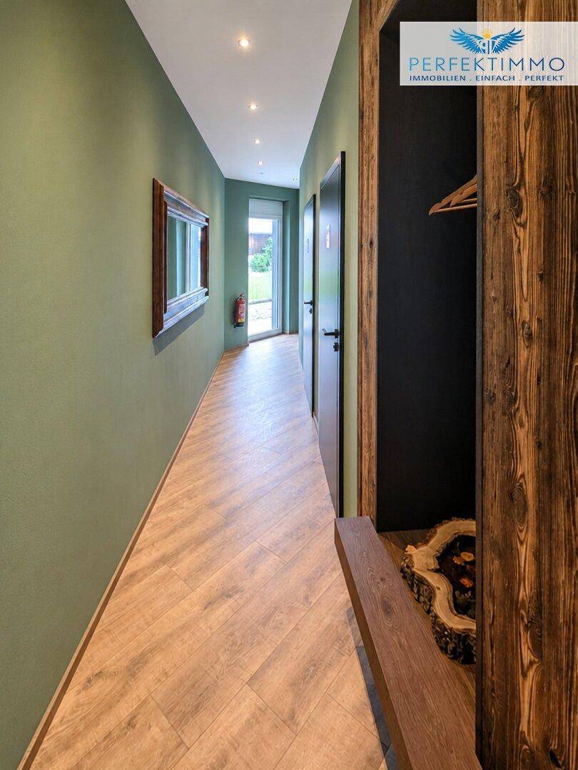 Heller Flur mit Holzboden, grünen Wänden und Zugang zu weiteren Räumen und dem Ausgang.