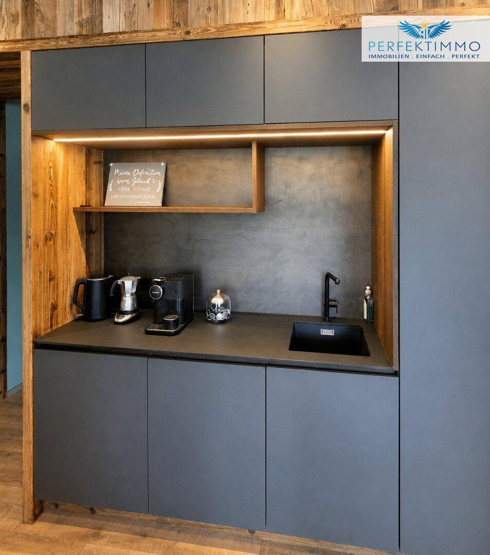 Kompakte Küchenzeile mit dunklen Schränken, Spüle und Kaffeemaschine, umgeben von Holz.