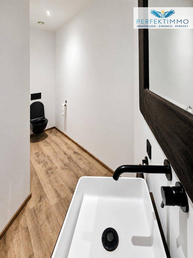 Modernes Gäste-WC mit weißem Waschbecken, schwarzer Toilette und Holzboden.