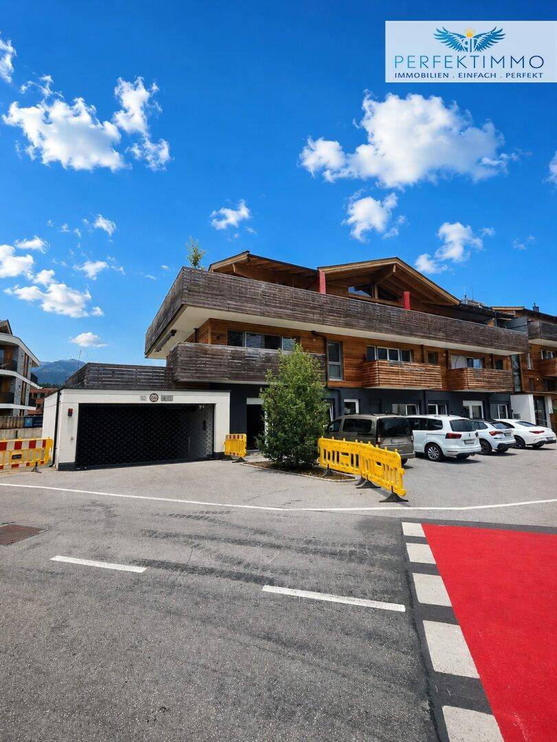 Modernes Gebäude mit Holzfassade, Tiefgarageneinfahrt und Parkplätzen im Freien.