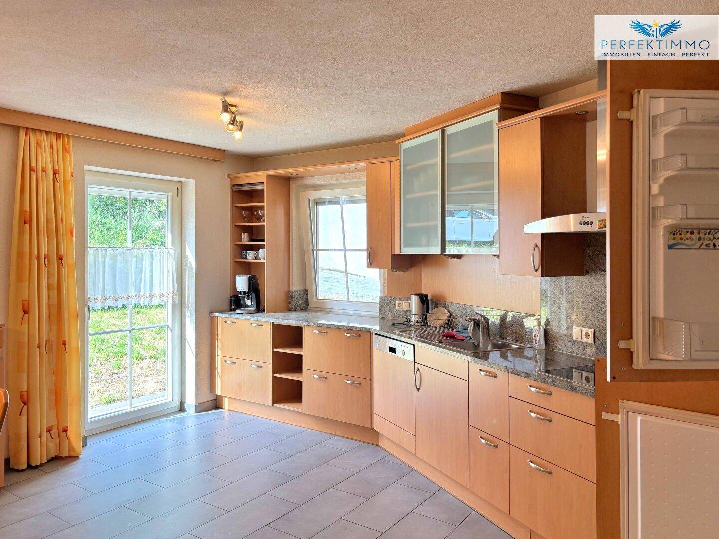 Helle Küche mit Holzschränken, Granitarbeitsplatten und Zugang zum Außenbereich.