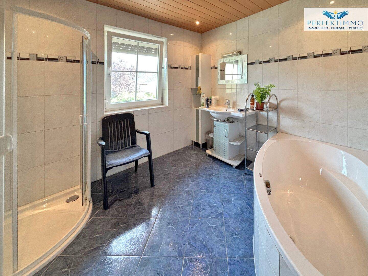 Geräumiges Badezimmer mit blauen Fliesen, Dusche, Eckbadewanne und Fenster.