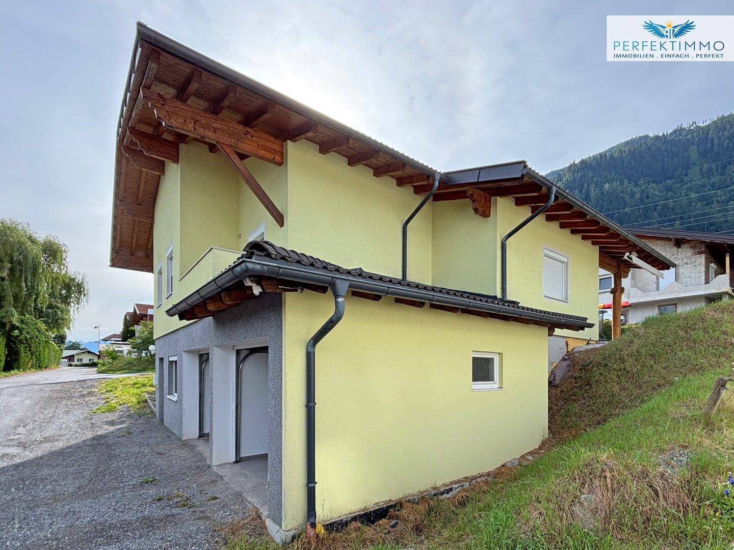 Seitenansicht des Hauses mit Doppelgarage im Untergeschoss und Bergblick.