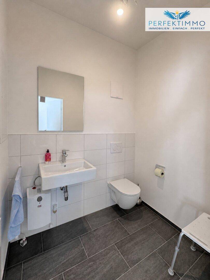 Modernes Gäste-WC mit dunklen Fliesen, wandhängendem WC und einem kleinen Waschbecken mit Spiegel.