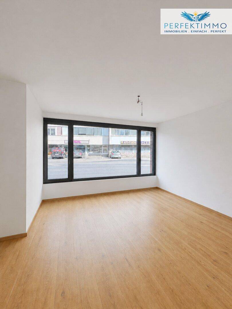 Heller Wohnraum mit Holzboden und breiten Fenstern, die einen Blick auf die belebte Straße ermöglichen.