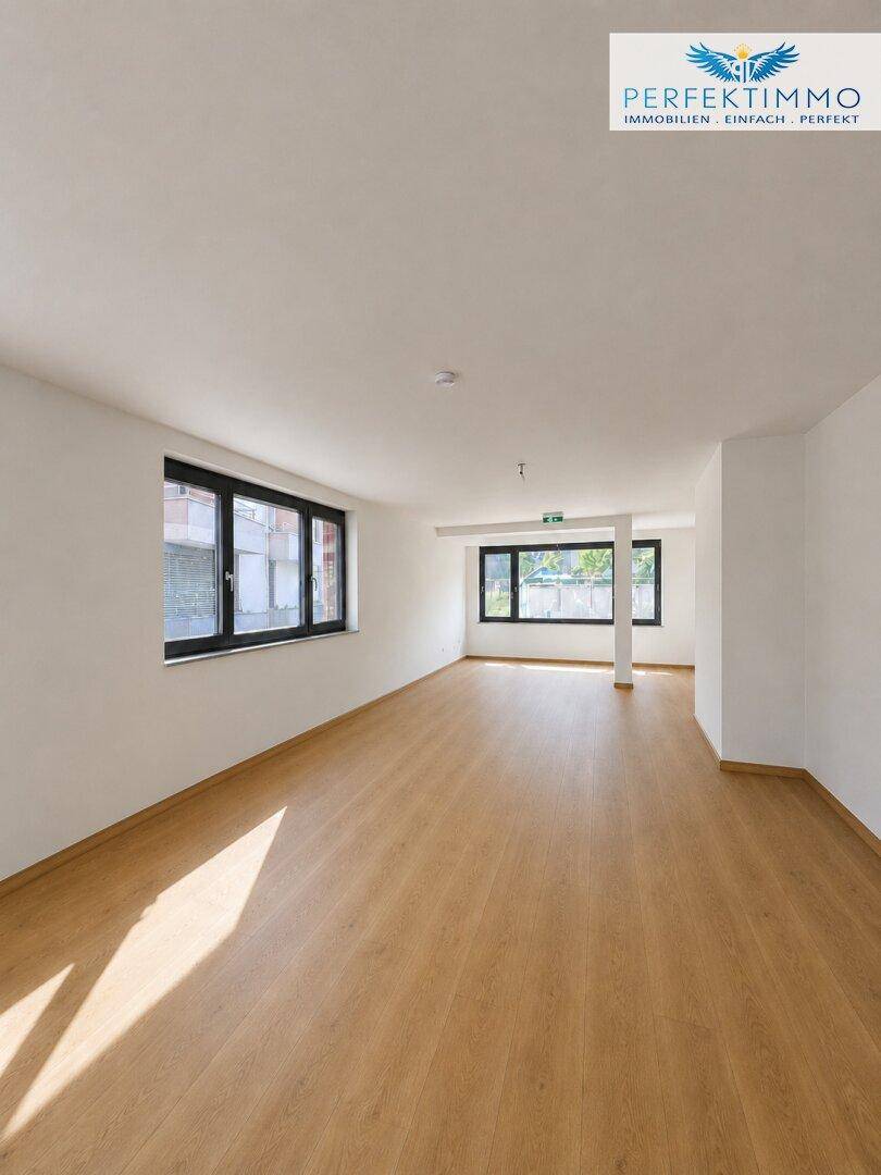 Geräumiger, heller Raum mit Holzboden und mehreren Fenstern, die für eine angenehme Atmosphäre sorgen.