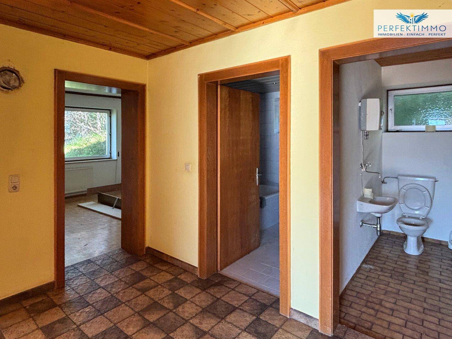 Flur im Originalzustand mit Holztüren und Holzdecke, der zu Bad und weiteren Zimmern führt.
