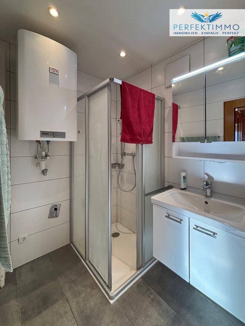 Modernes Badezimmer mit Duschkabine, Waschbecken und Warmwasserboiler an der Wand.