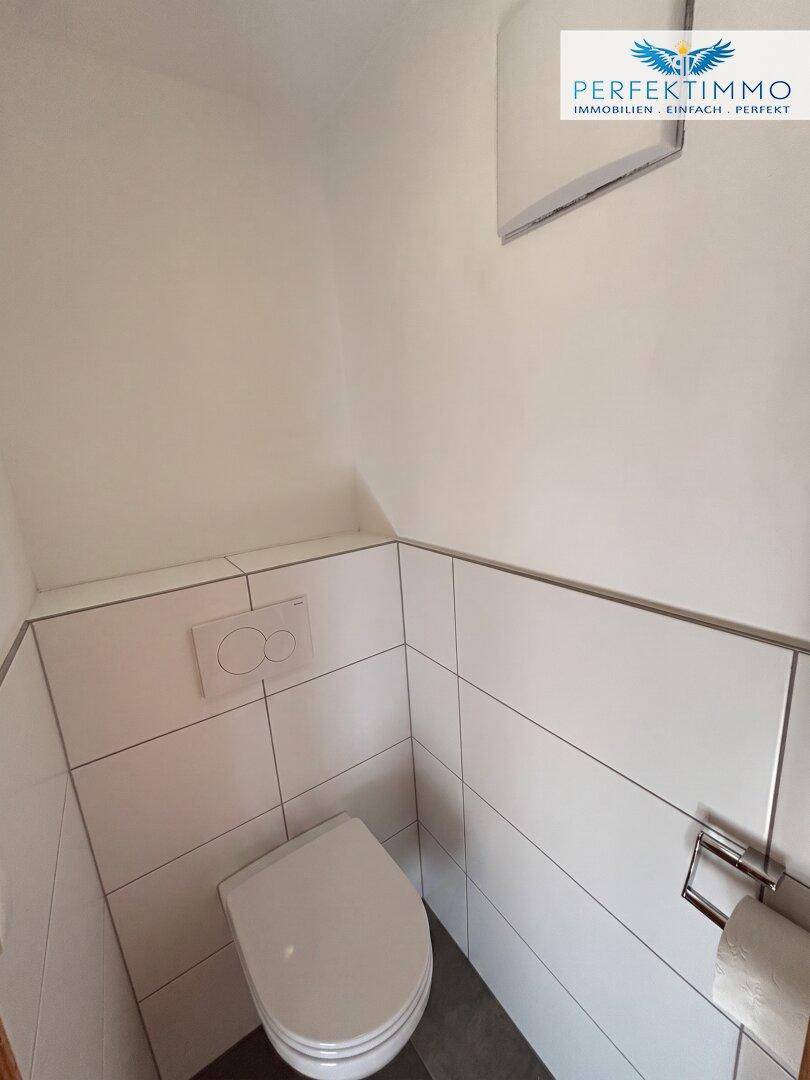 Kleines separates WC mit wandhängender Toilette und weißen Fliesen an den Wänden.