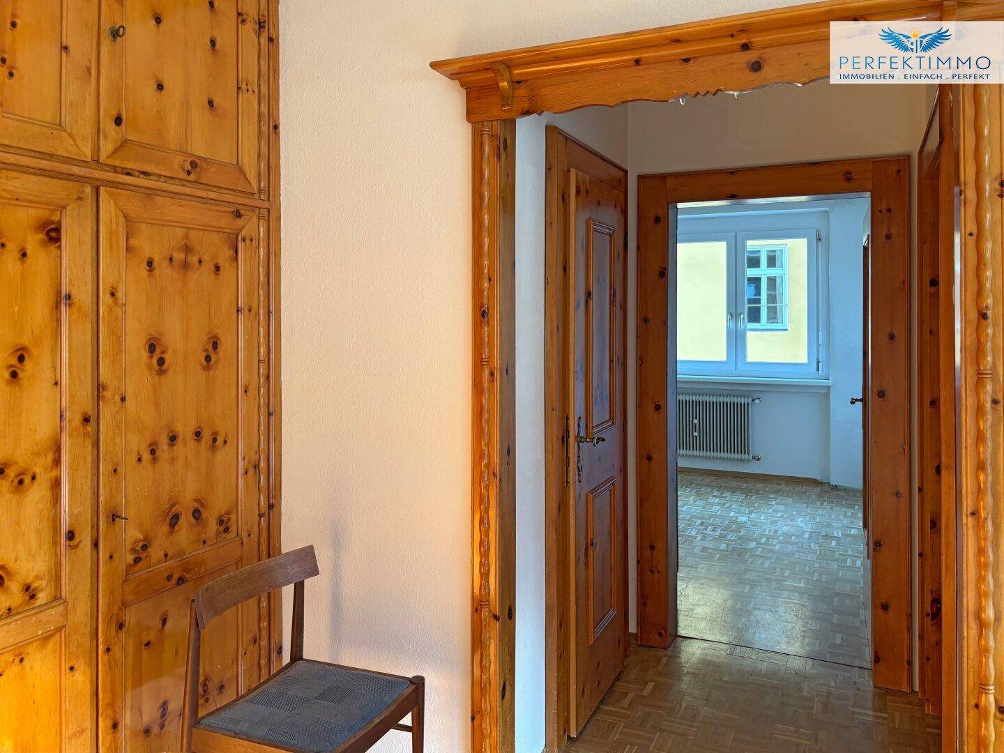 Flur mit Einbauschränken aus Holz und klassischem Parkettboden, der zu weiteren Räumen führt.