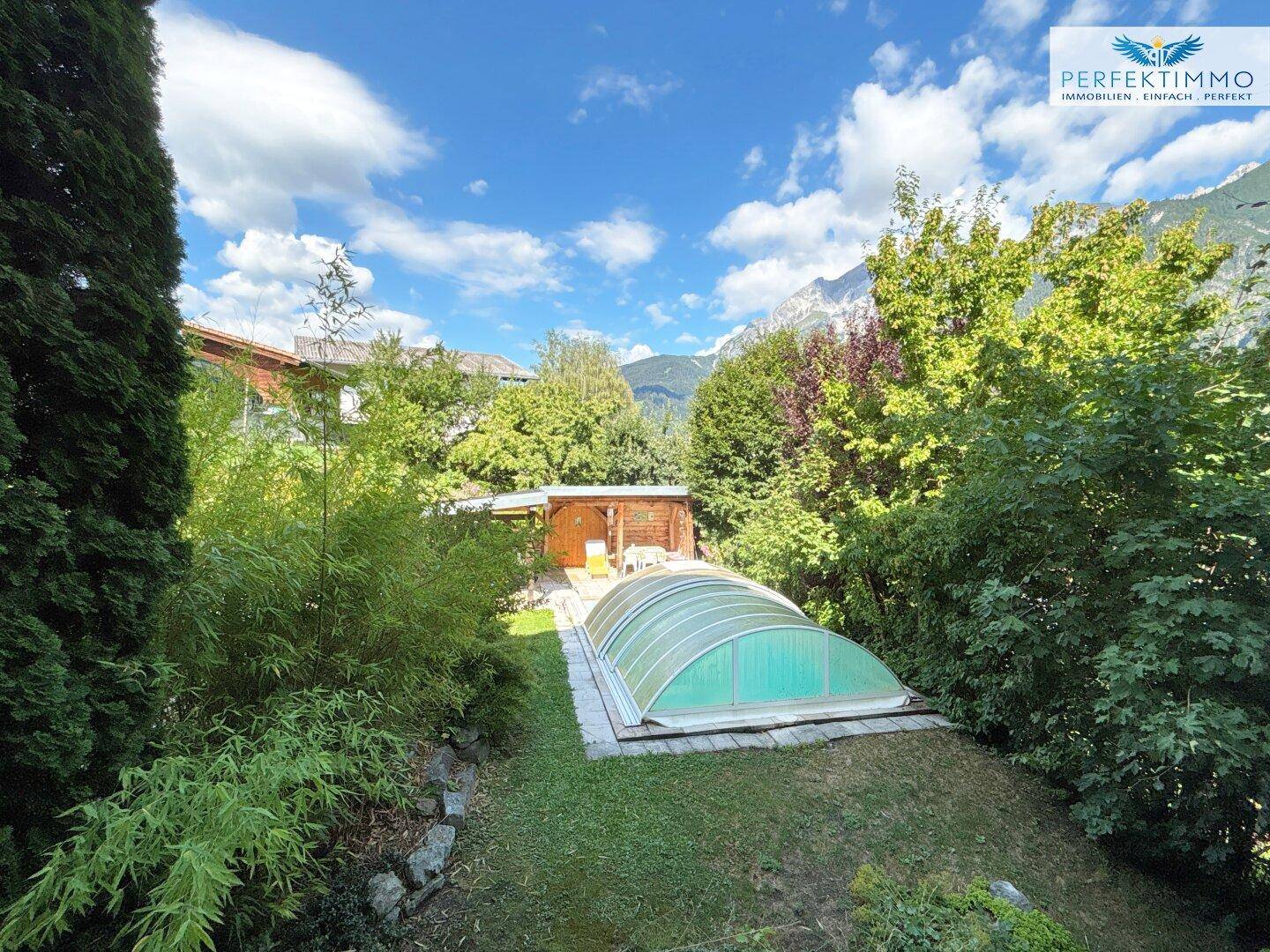 Großer Garten mit Rasenfläche, Bäumen und einem überdachten Poolbereich.