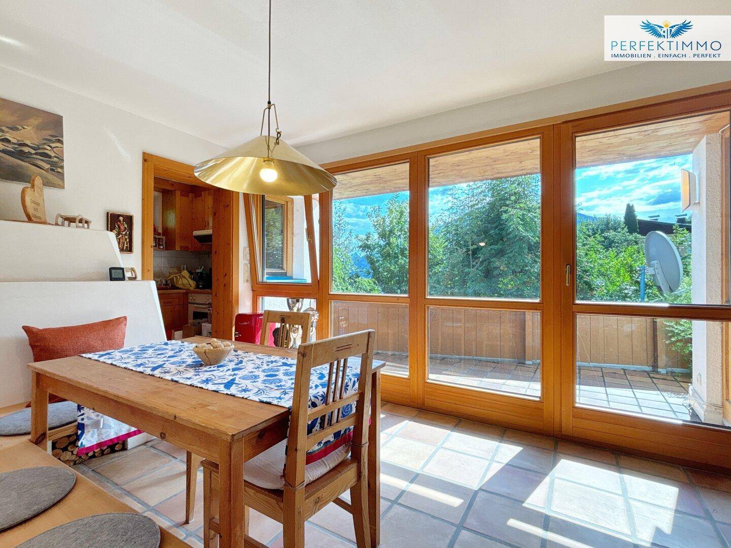 Essbereich mit Holztisch, Terrakottafliesen und weitem Blick ins Grüne durch große Fenster.