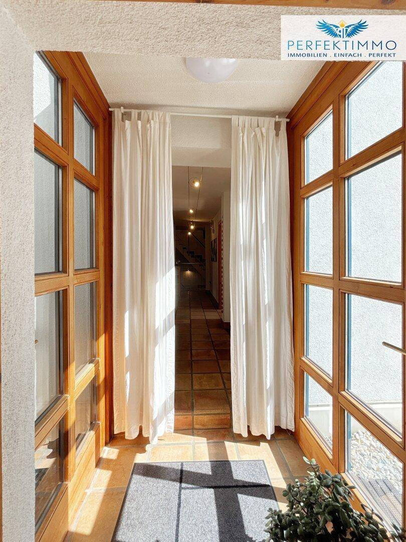 Heller Eingangsbereich mit großen Fenstern, Terrakottafliesen und Blick in den Flur.