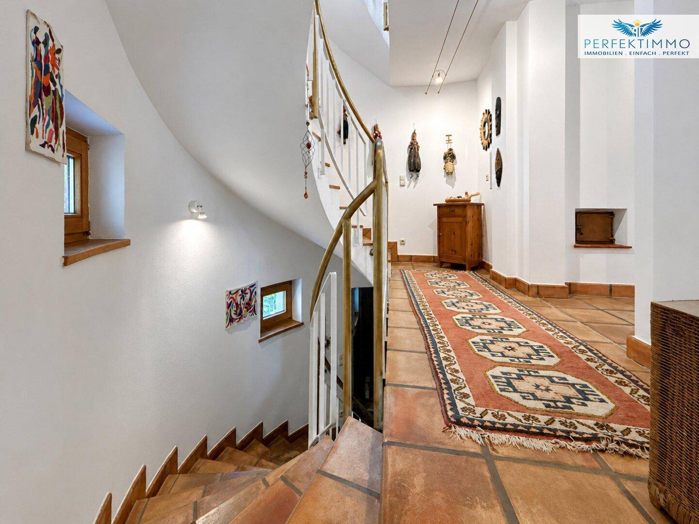 Geschwungene Treppe mit Terrakottafliesen und dekorativen Elementen in einem hellen Flur.