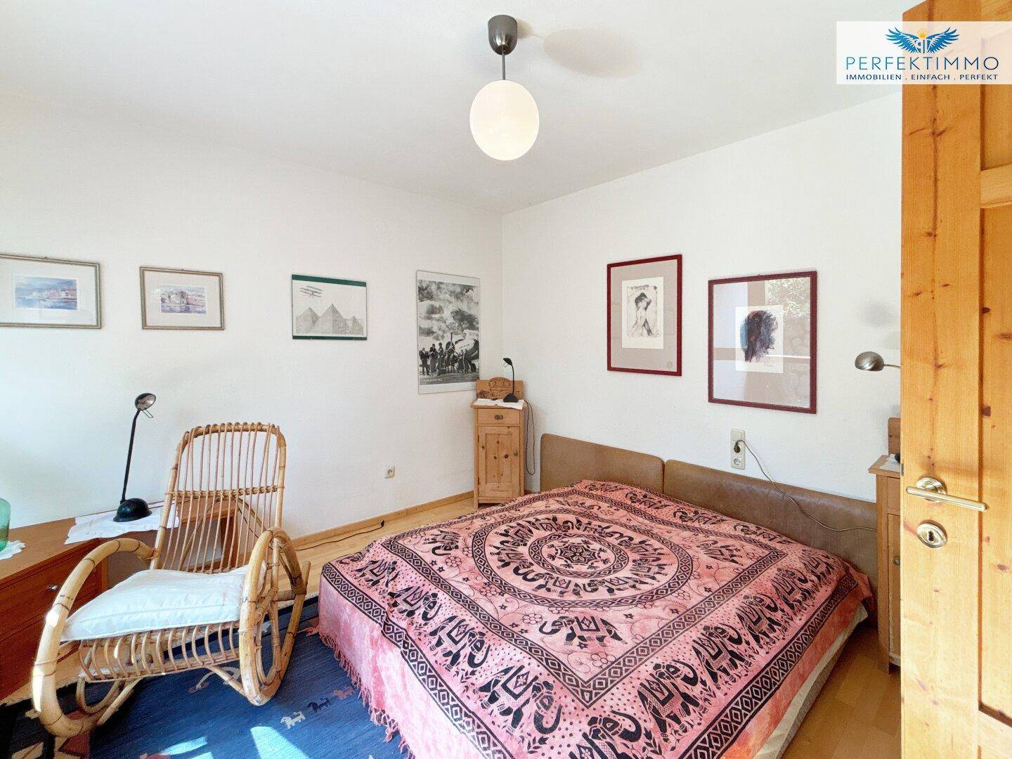 Schlafzimmer mit Doppelbett, Rattansessel und Bildern an den Wänden, hell und gemütlich.
