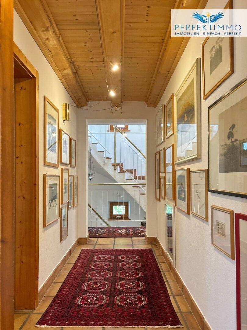 Langer Flur mit Terrakottafliesen, Holzbalkendecke und Blick auf die Treppe.