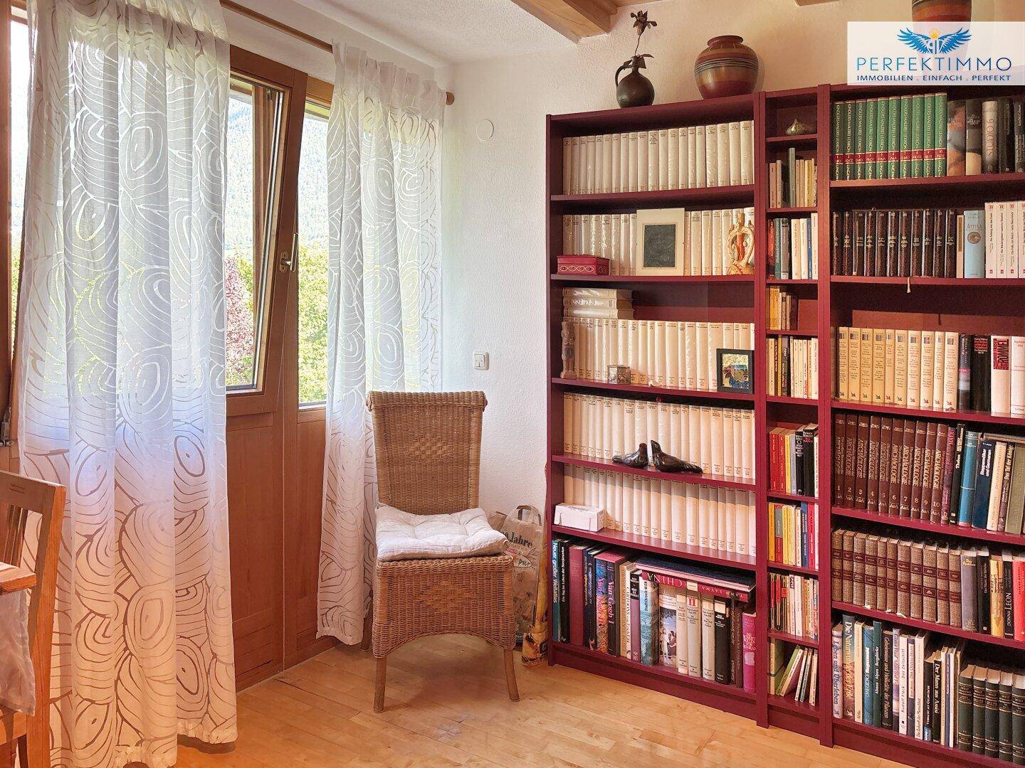 Heller Wohnbereich mit großen Bücherregalen und Blick ins Grüne durch die Fenstertür.
