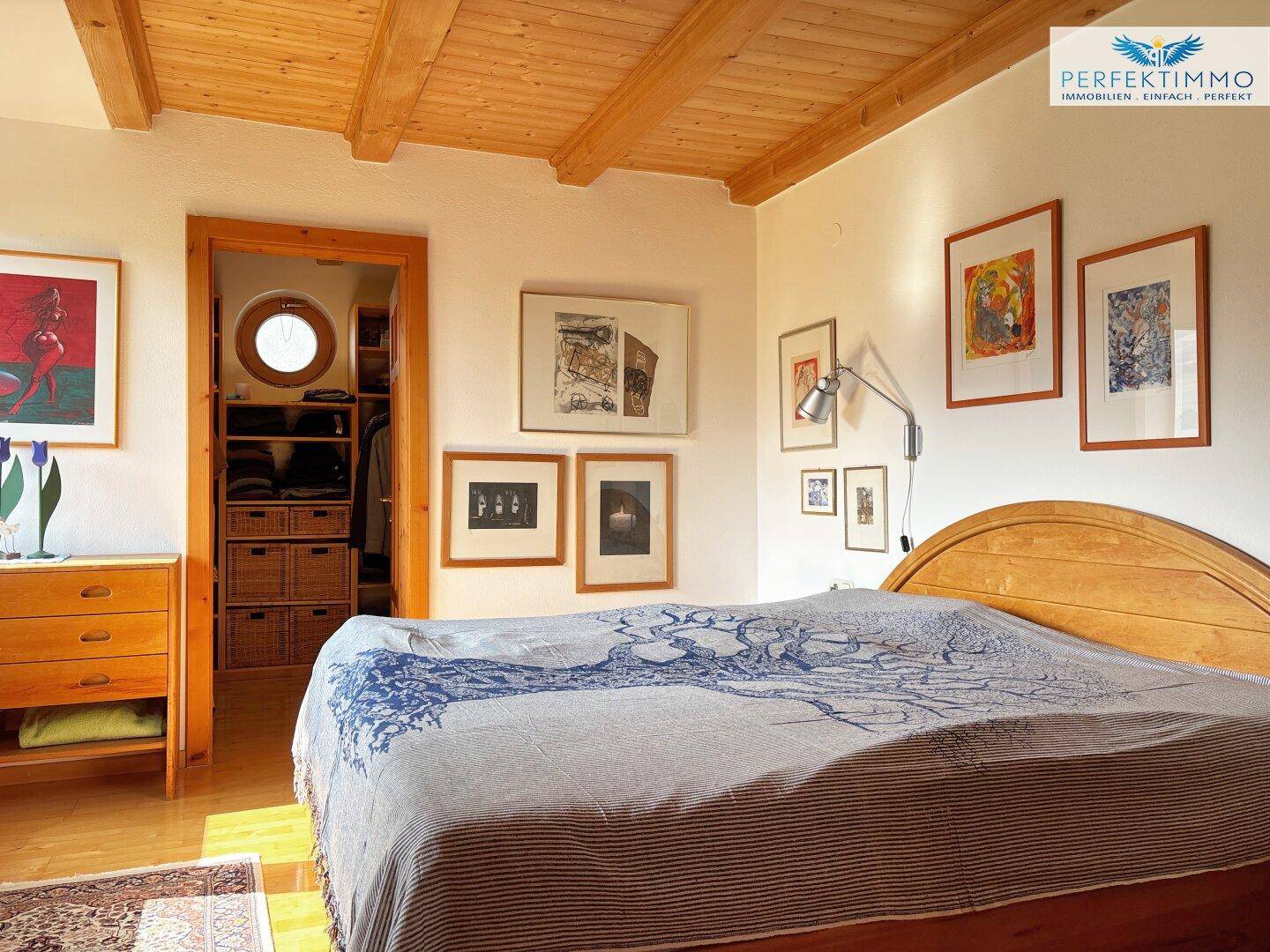 Gemütliches Schlafzimmer mit Holzbett, Kunstwerken und Zugang zu einem begehbaren Kleiderschrank.